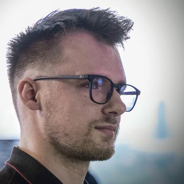 Side profile of a man with short dark hair and glasses, looking to the right.
